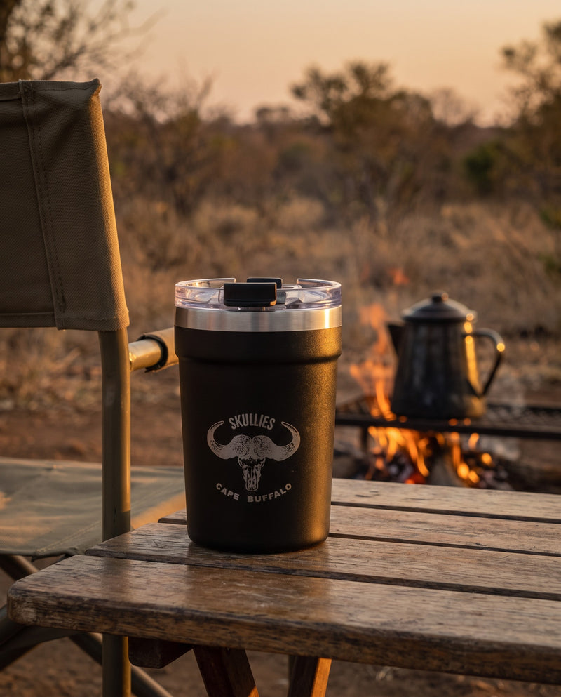 Load image into Gallery viewer, Black Cape Buffalo Skullies Coffee Cup on a bush camp table by the fire
